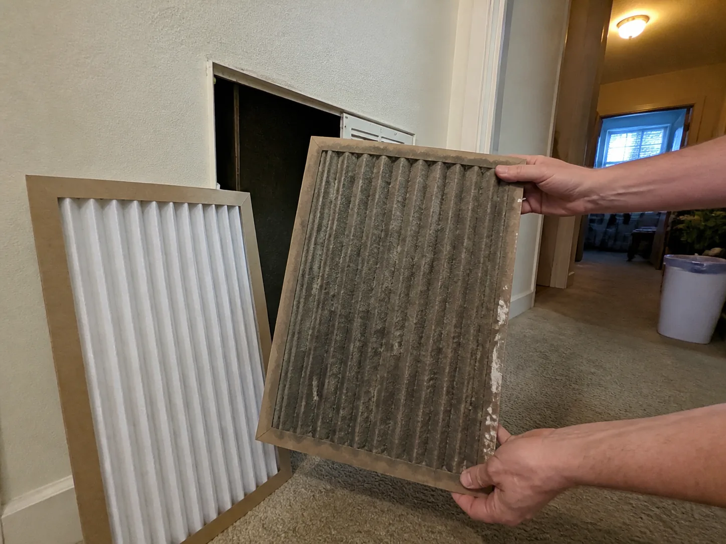 Dirty HVAC filter held beside a clean replacement at an open return grille